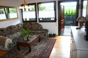 Ferienhaus EifelNest Wohnzimmer Fernsicht Auch durch die große Fensterfront des Wohnzimmers genießen Sie die Fernsicht. Eine komfortable Sitzecke (m. Schlaffunktion) lädt zum gemütlichen Erzählen, Planung von Ausflügen oder einfach zum Entspannen ein.