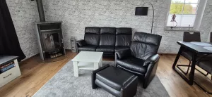 Gemütliches Wohnzimmer, frisch renoviert und neuer echt Holzboden Februar 2026 mit Sofa, Fernsehsessel mit Fußhocker und Kaminofen.
