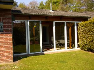 Die bodentiefen Fenster des Wintergartens lassen sich komplett zur Seite schieben; so entsteht ein luftiger regengeschützter Freisitz.