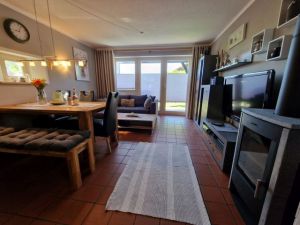 Wohnzimmer mit Essbereich Offene Küche. Wohnzimmer mit Schlafcouch für zwei Personen und Couchtisch, Wohnzimmerwand, Esstisch mit Sitzbank und drei Stühlen, Kaminofen. Zur Unterhaltung stehen ein Flachbild-TV mit Sat-Empfang, ein DVD-Player und ein Radio zur Verfügung.