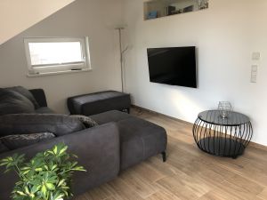 In dem Wohnbereich gibt es eine bequeme Couch, einen Hocker und einen Fernsehapparat, um gemütlich zusammen zu sitzen oder Fernseh zu schauen.