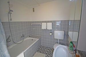 hat eine Badewanne mit Duschvorhang, ein Waschbecken, WC und einen Handtuchwärmer.