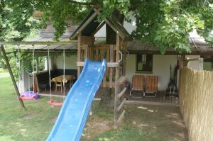 Im Garten befinden sich 2 Schaukel, eine Rutsche und ein Sandkasten mit Spielwaren. Dahinter sehen Sie die große, schattige Terrasse.