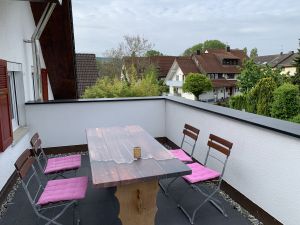 Mit Tisch und Stühlen und großem Sonnenschirm.