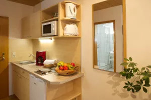 Kleine Küchenzeile mit Ceranfeldkochfeld, Kühlschrank mit Gefrierfach, Teller, Tassen Gläser, Besteck, Töpfe, Kochutensilien, Kaffeemaschine, Wasserkocher, Toaster, Geschirrtücher